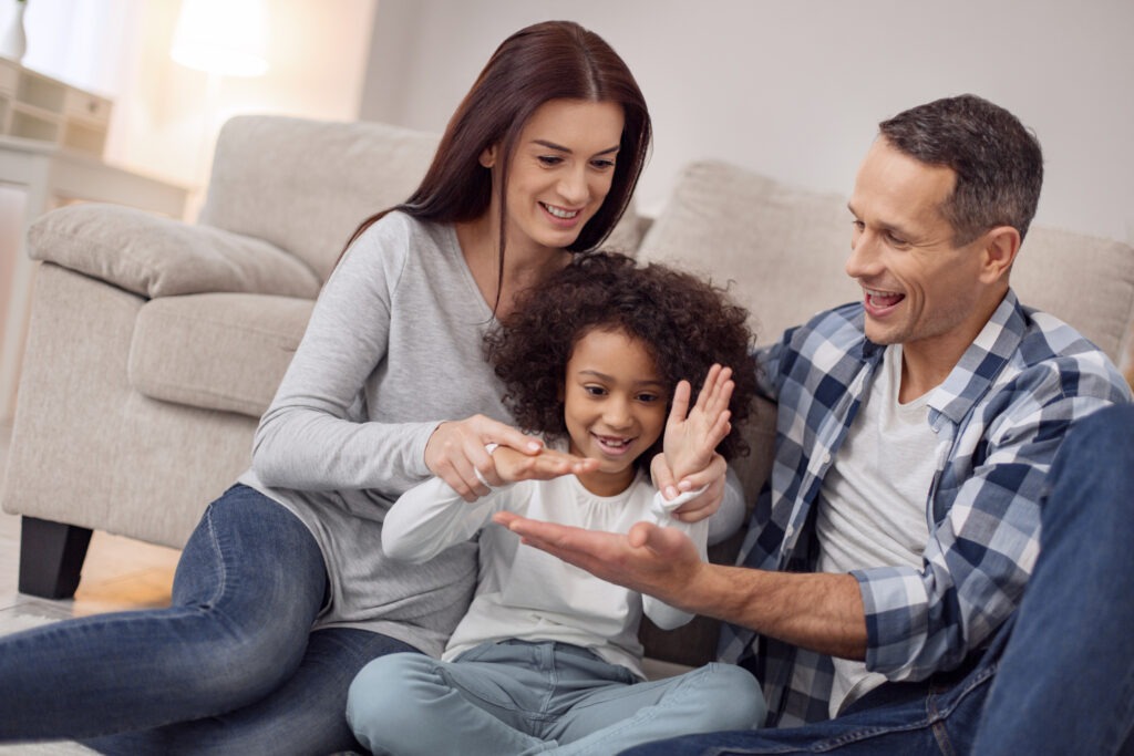 Inspired family. Pretty inspired curly-haired smiling and having fun with her parents while they all sitting on the floor navigate the complexities of adoption